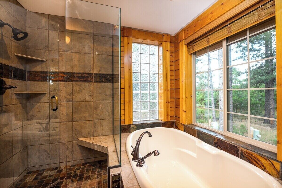 A bathroom with a freestanding bathtub, a shower area with a glass door, and a window with a view of trees.