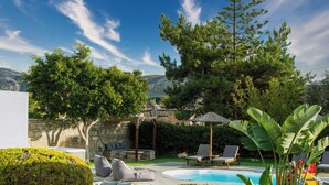 Un giardino con piscina, sedie a sdraio e un muro in pietra.
