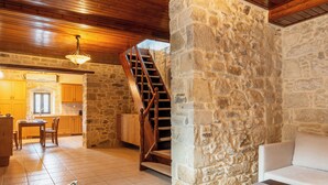 Un'ampia zona giorno con parete in pietra, scala in legno e sala da pranzo con tavolo e sedie.