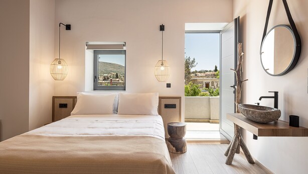 Una camera da letto con un letto, lampade da comodino, una finestra vista, uno specchio rotondo e un tavolino in legno con lavabo a incasso.
