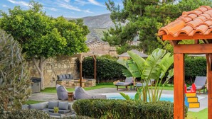 Un cortile con un muro in pietra, un pergolato in legno, una piscina e mobili da esterno.