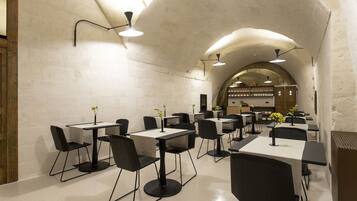Un comedor moderno con paredes blancas, sillas y mesas negras, que cuenta con un techo abovedado central e iluminación colgante.