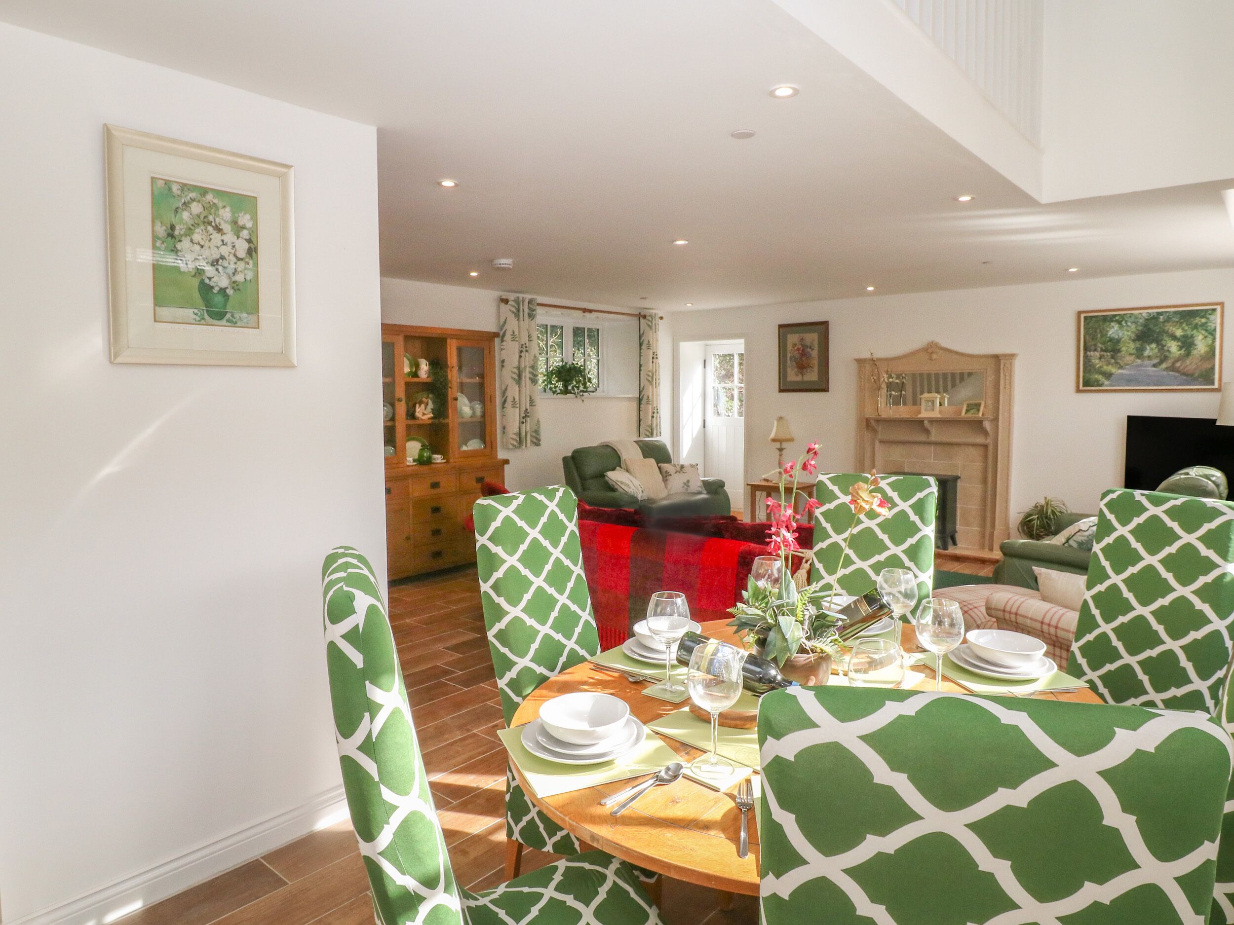 Een eetgedeelte met groene gestreepte stoelen, een houten tafel gedekt voor een maaltijd, en een woonkamer op de achtergrond met een open haard.