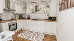 Une cuisine moderne avec des meubles blancs, un plan de travail en bois, un four encastré, un four à micro-ondes et une fenêtre avec des rideaux.