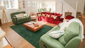 Un salon spacieux avec un canapé vert, un canapé rouge et une table basse en bois. Un escalier mène à un autre niveau.