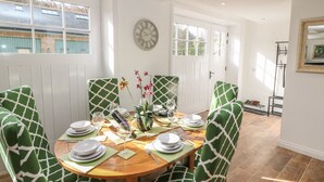 Un coin repas avec une table ronde en bois, des chaises à motifs verts et une horloge au mur.