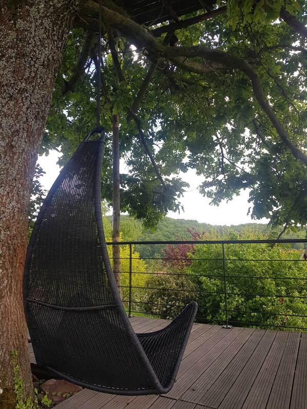 A hanging chair on a wooden deck with a view of a lush green landscape. - On your terrace at the foot of an oak tree, feel the Alsace's vibes ! (Barr)
