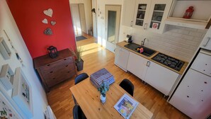A compact kitchen with white cabinets, a wooden dining table, and a red accent wall. - On your terrace at the foot of an oak tree, feel the Alsace's vibes ! (Barr)