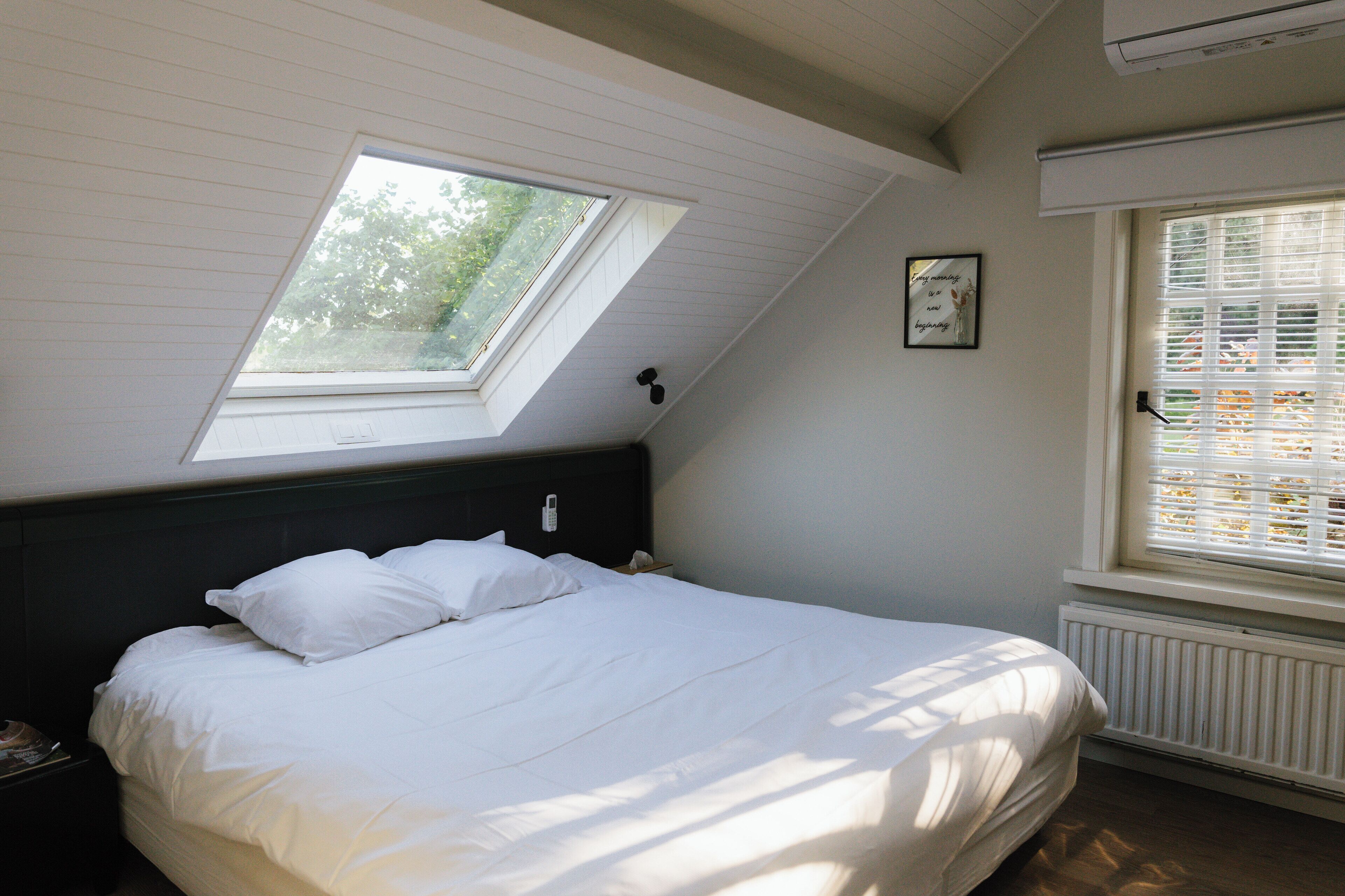 Un dormitorio con tragaluces, una cama, una mesita de noche y una ventana con persianas.
