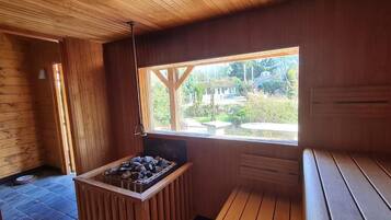 Une cabane en bois avec une cheminée en pierre, un banc et une fenêtre donnant sur un jardin.