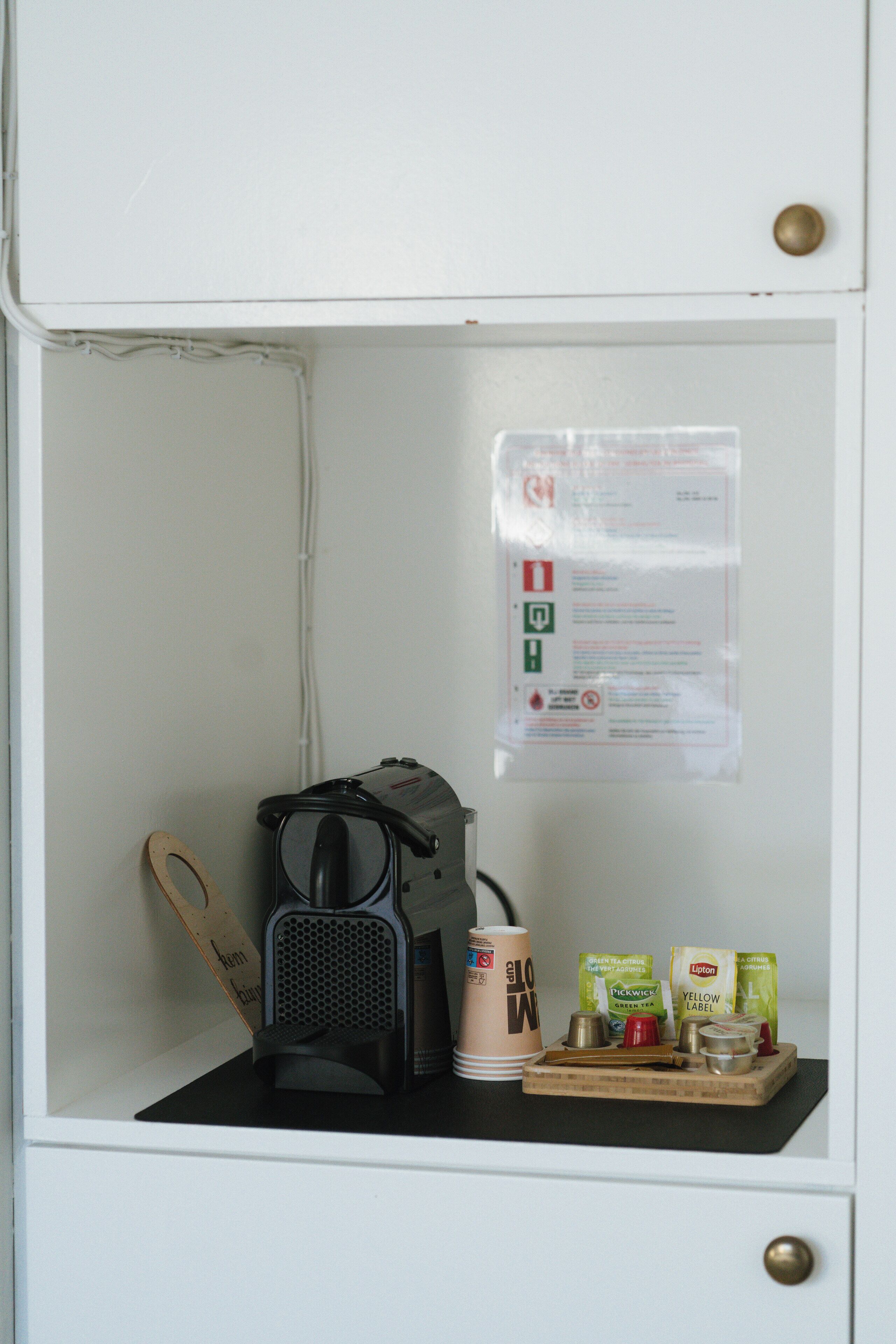 A small kitchenette with a coffee maker, a cup, and some tea packets.