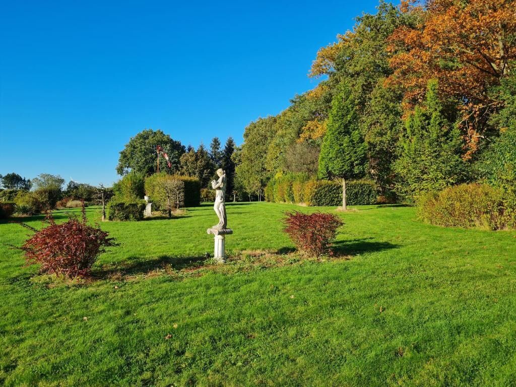 A well-maintained garden with a statue, neatly trimmed hedges, and a variety of trees in the background.