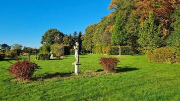 A well-maintained garden with a statue, neatly trimmed hedges, and a variety of trees in the background.