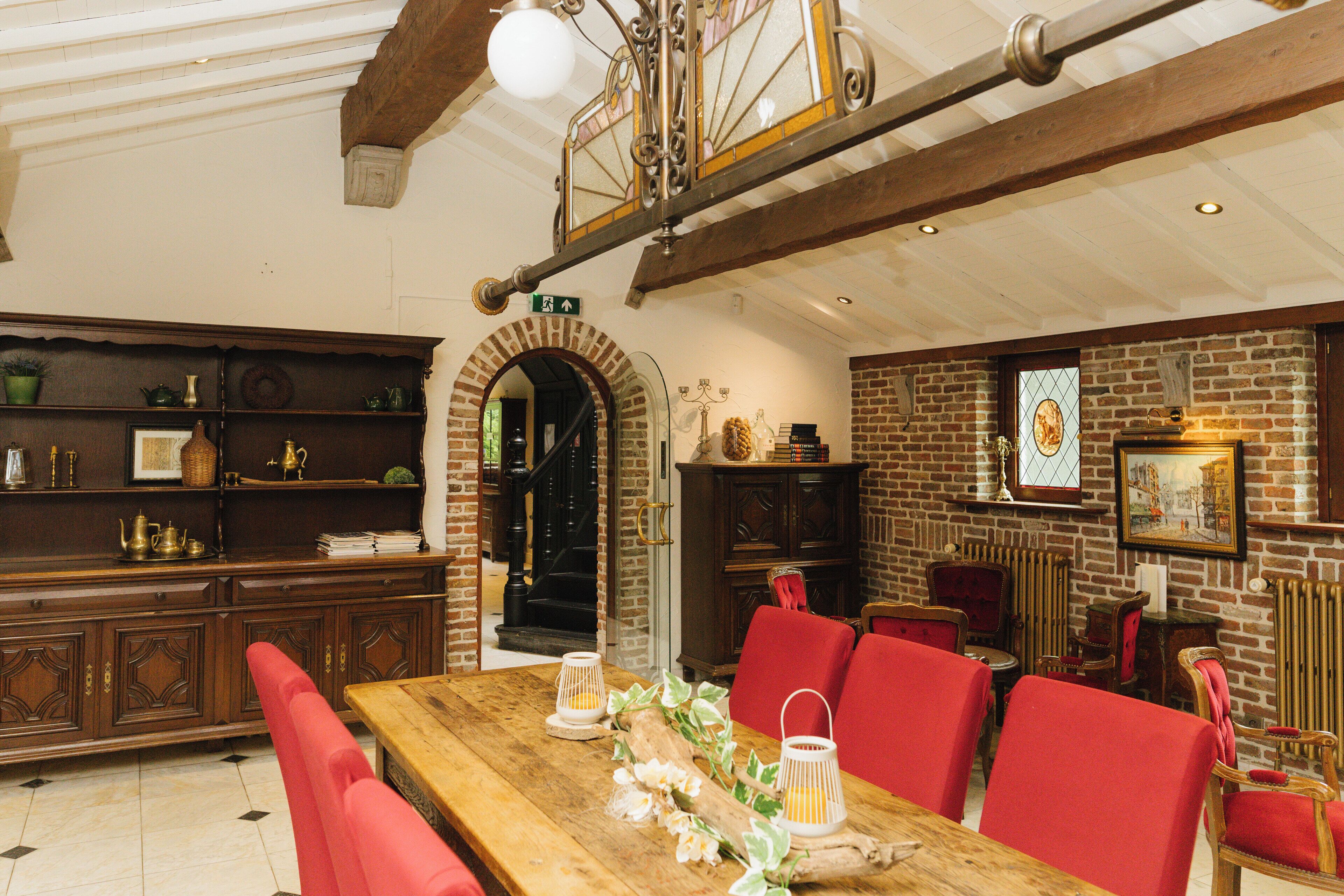 A dining area with a wooden table, red chairs, and a brick wall with a fireplace.