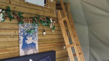 Ein Schlafzimmer mit einer Wand aus Holzlattung, einem Bett mit weißer und blauer Bettwäsche, einer Leiter und Lichterketten.