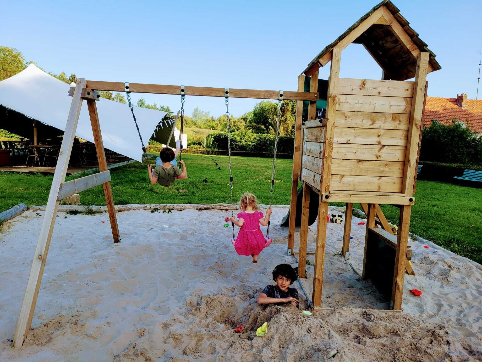 Un columpio de madera con un arenero y una pequeña construcción de madera.