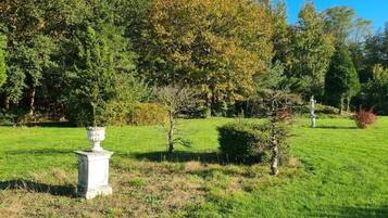 A well-maintained lawn with a white urn and a statue in the foreground, surrounded by trees and shrubs.