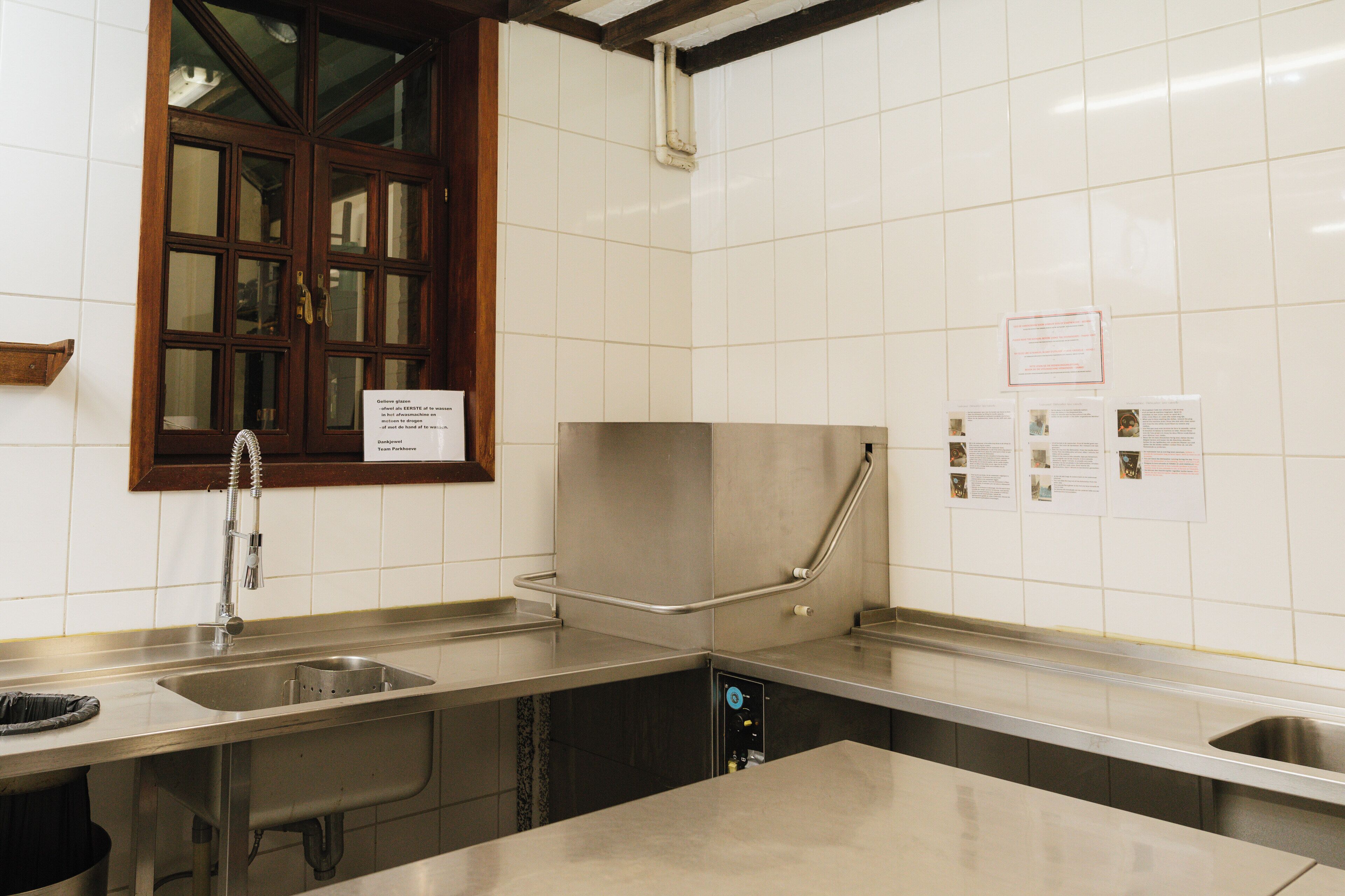 A kitchen with stainless steel countertops, a sink, and a window with a wooden frame.