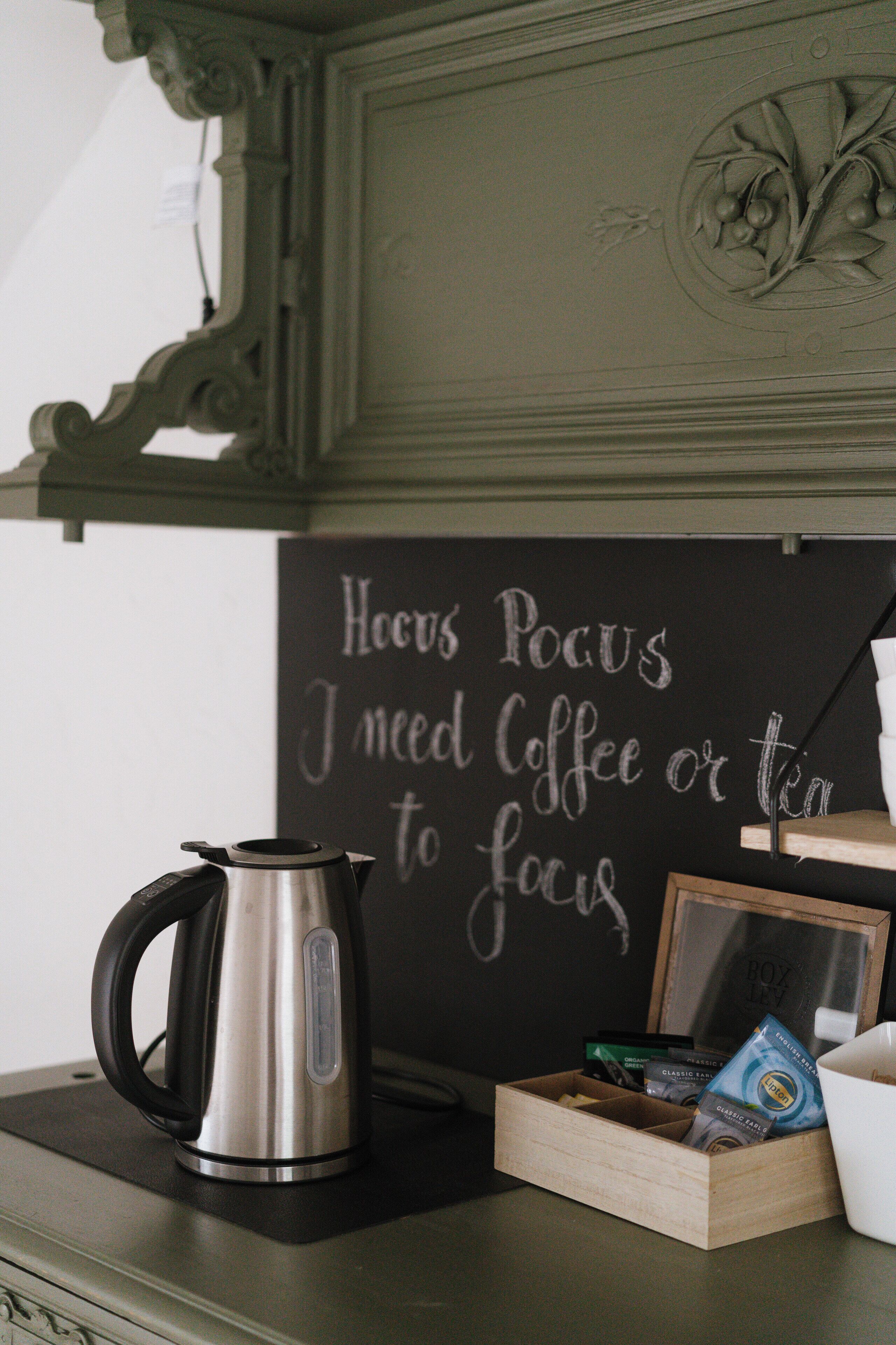 A coffee maker, a wooden box with coffee packets, and a chalkboard with a motivational message.