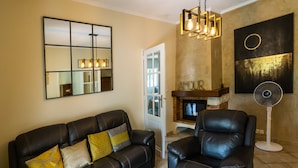 A living room with a leather sofa, a leather armchair, a glass coffee table, a fireplace, and a large mirror.