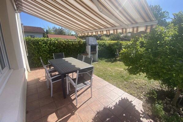 An outdoor patio with a table and chairs, a grill, and a covered area.