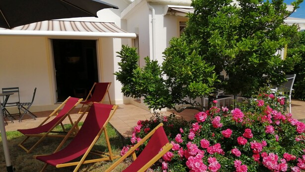 Outdoor seating with red cushions, a white building, and a bush of pink flowers.