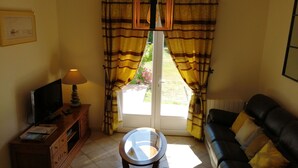 A living room with a television, a lamp, a glass-top coffee table, a sofa, and a window with curtains.