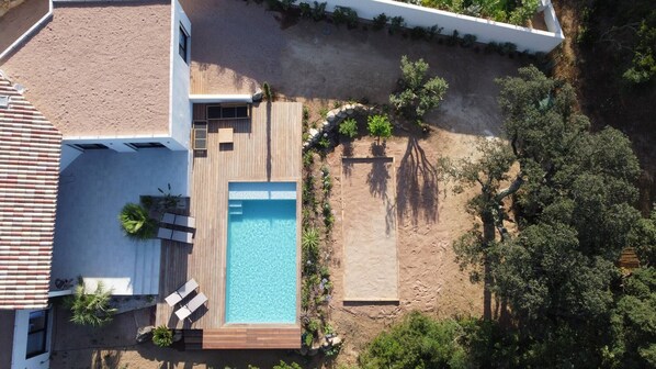 An aerial view of a property with a swimming pool, wooden deck, and surrounding greenery.