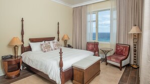 Ein Hotelzimmer mit einem großen Bett, zwei Nachttischen, einem Sessel und einem kleinen Tisch, mit Blick aufs Meer.