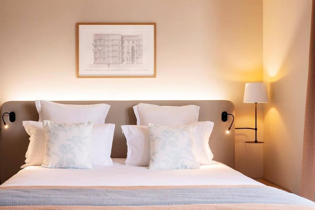 Een hotelkamer met een bed, kussens, een lijst met een foto aan de muur en een bedlamp.