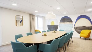 Una sala conferenze con un tavolo rotondo, sedie color verde acqua, una sedia gialla, un grande specchio e opere d'arte astratte alle pareti.