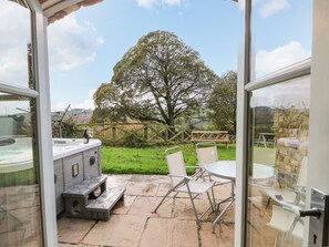 An open patio with a hot tub, outdoor seating, and a view of a large tree and grassy area.