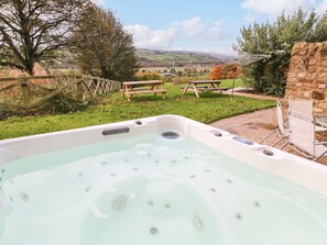 A hot tub with a view of a countryside landscape, a wooden fence, and a stone wall.