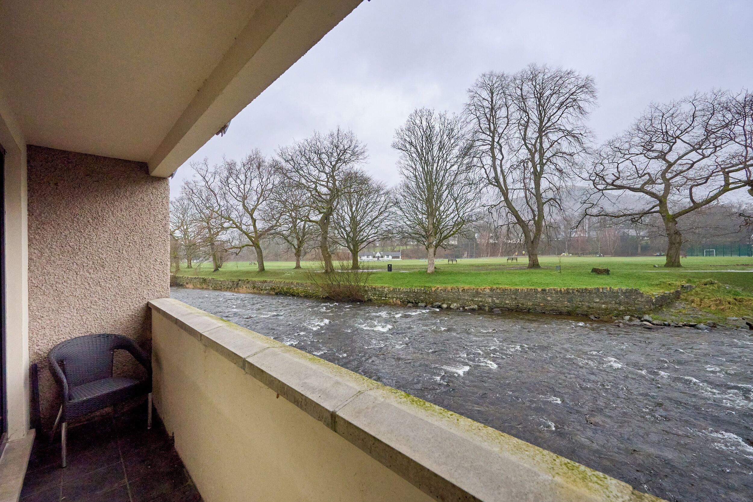 A balcony with a view of a river, trees, and a grassy area.