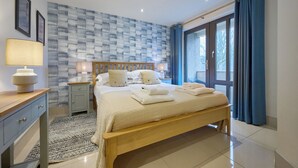 Une chambre à coucher avec un lit en bois, des tables de chevet, une commode, un mur à motifs et une vue à travers une porte vitrée.