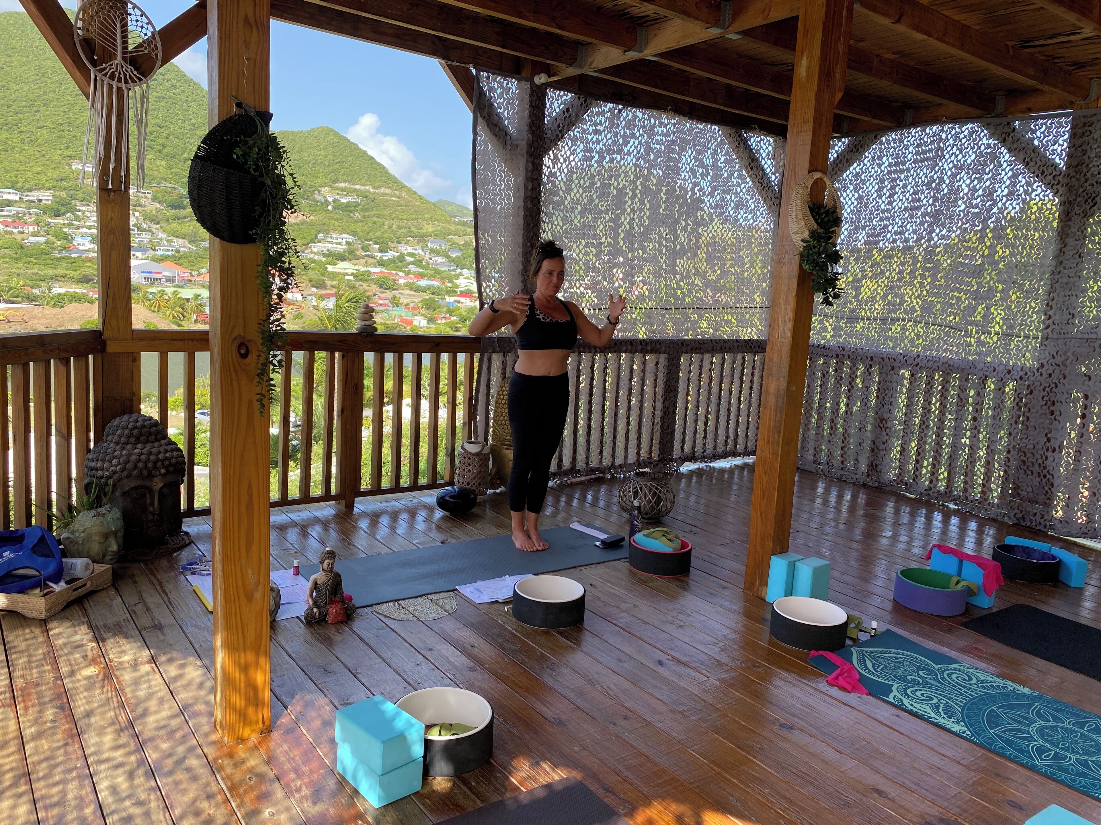 Um deck de madeira com tapetes de yoga e almofadas de meditação, com vista para uma paisagem montanhosa.