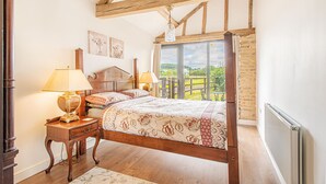A bedroom with a four-poster bed, wooden headboard, and a view of a green landscape through a large window. - Countryside Retreat/Panoramic Picturesque Views (Chippenham)