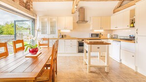 A kitchen with wooden beams, white cabinets, a dining table with chairs, and a view through a glass door. - Countryside Retreat/Panoramic Picturesque Views (Chippenham)