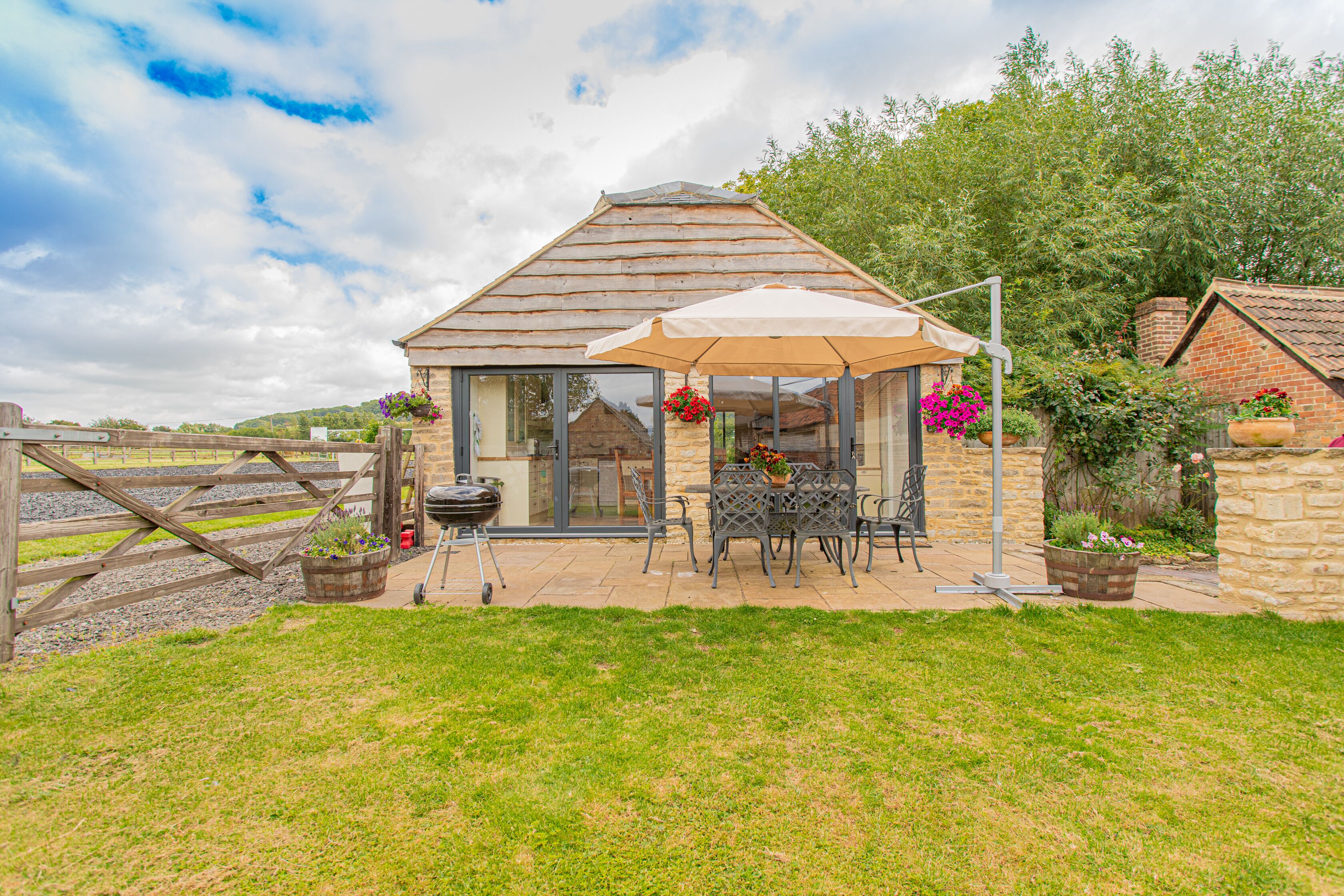 A cozy cottage with a patio, a table with chairs, and a hanging flower basket.