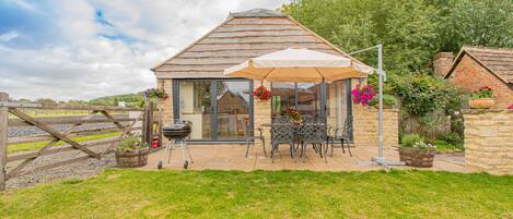 A cozy cottage with a patio, a table with chairs, and a hanging flower basket.