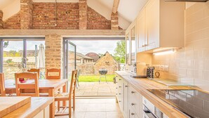 A kitchen with wooden cabinets, a glass countertop, and a view of the backyard. - Countryside Retreat/Panoramic Picturesque Views (Chippenham)