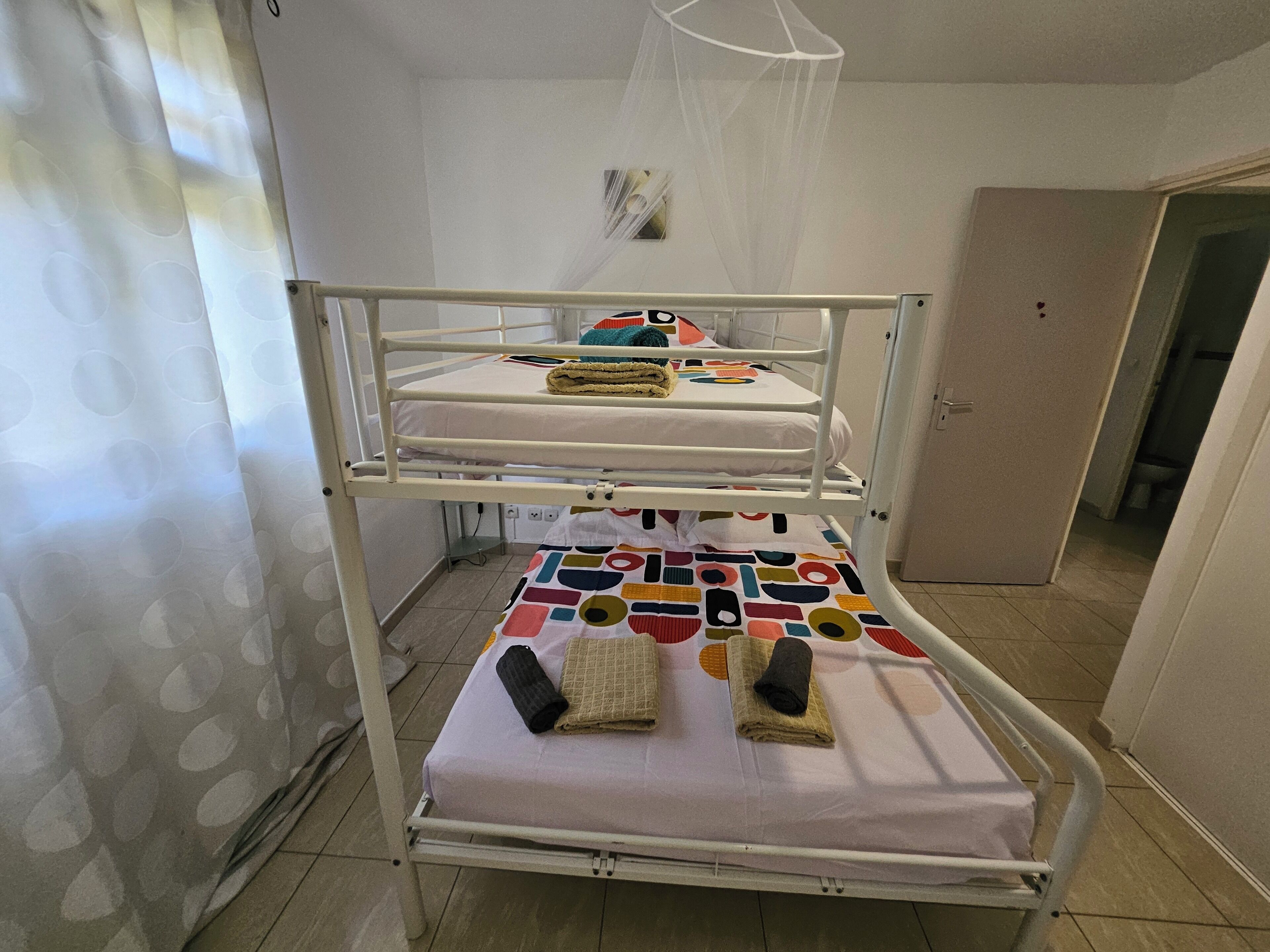 Ein Stockbett mit farbenfroher Bettdecke und Moskitonetz darüber.