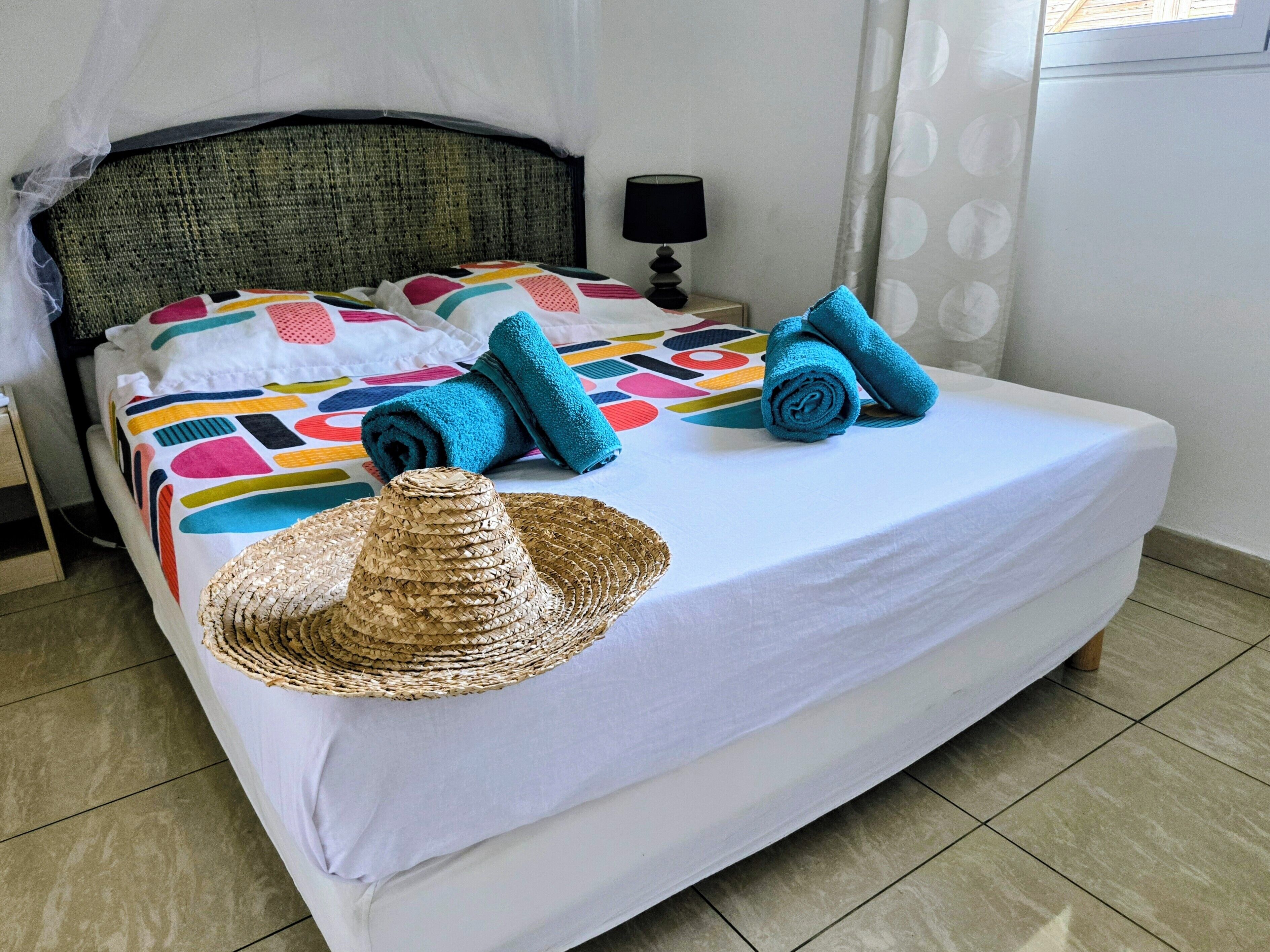 Una cama bien hecha con un edredón colorido, toallas enrolladas y un sombrero tejido sobre la cama.