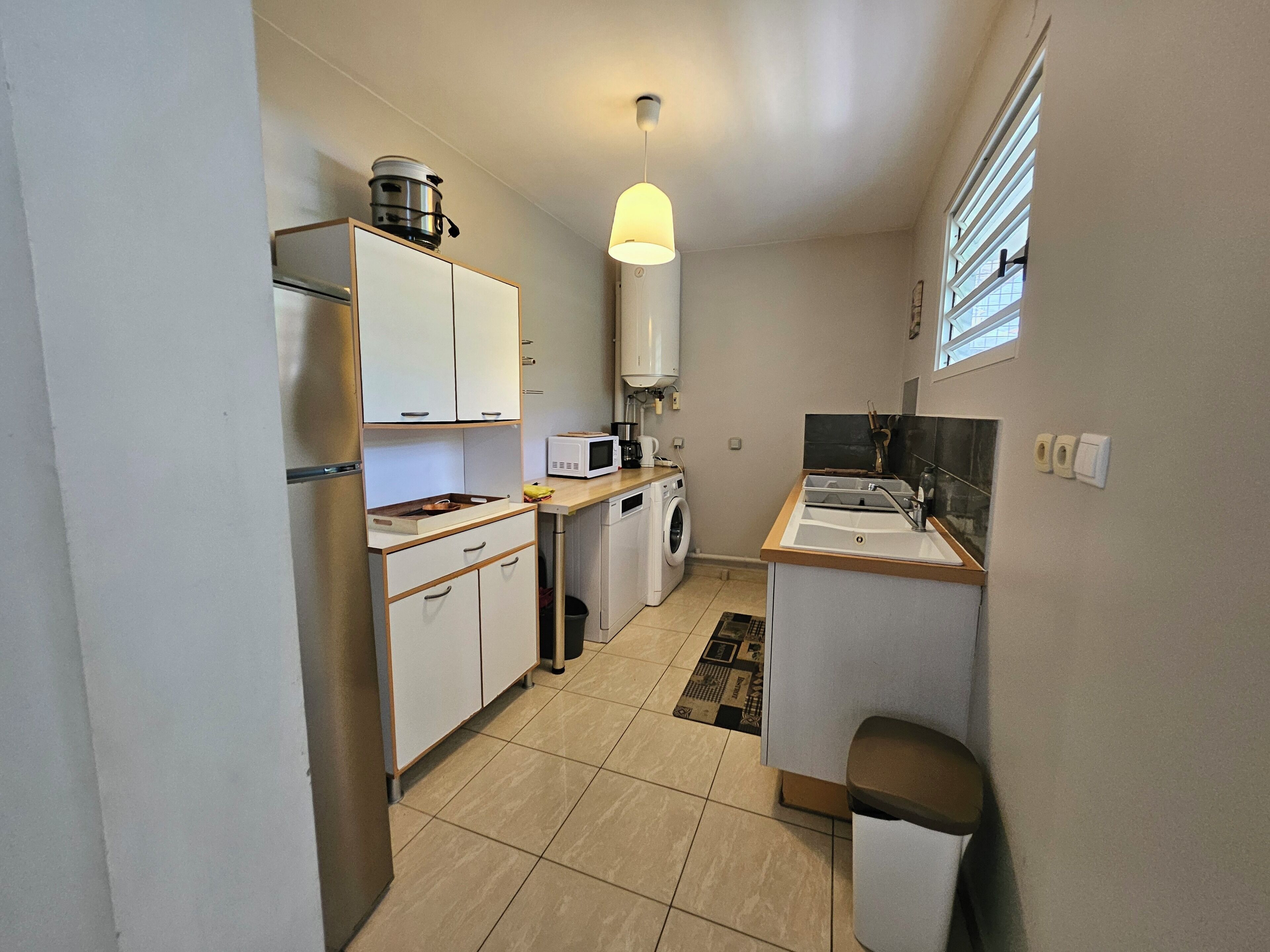 Cocina compacta con armarios blancos, microondas, lavadora y pileta.