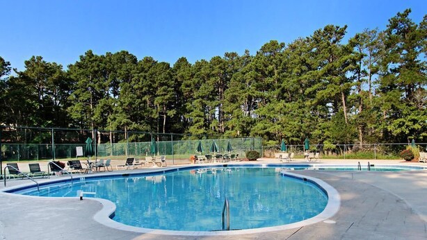 A swimming pool with lounge chairs and umbrellas, surrounded by a fence and trees.