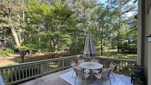 A covered patio with a round table and chairs, surrounded by a wooden deck and a view of a wooded area.