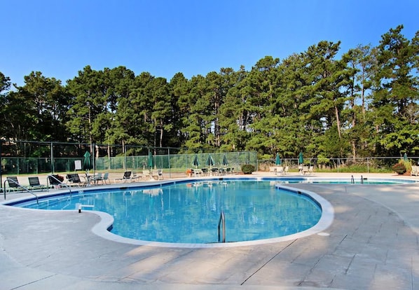 A swimming pool with lounge chairs and umbrellas, surrounded by a fence and trees.