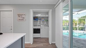 A kitchen with a countertop, a washing machine, and a dryer. There is a sign on the wall and a view of a swimming pool outside.