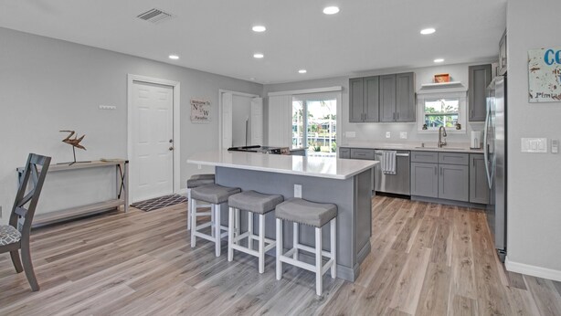 A modern kitchen with grey cabinets, a central island with bar stools, and a view to the outside.