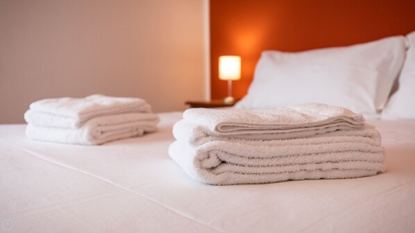 A neatly made bed with folded white towels and a bedside lamp.